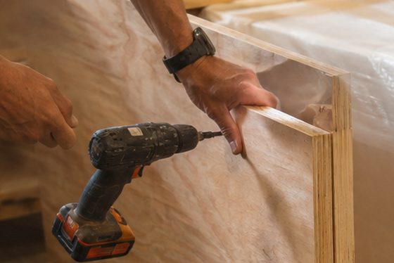 Hands driving a screw through a plywood panel while building a crate around a wrapped item