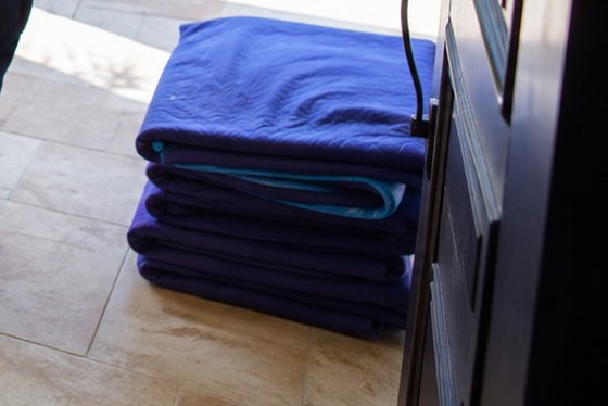 A stack of folded quilted moving blankets on a tiled floor beside an open doorway